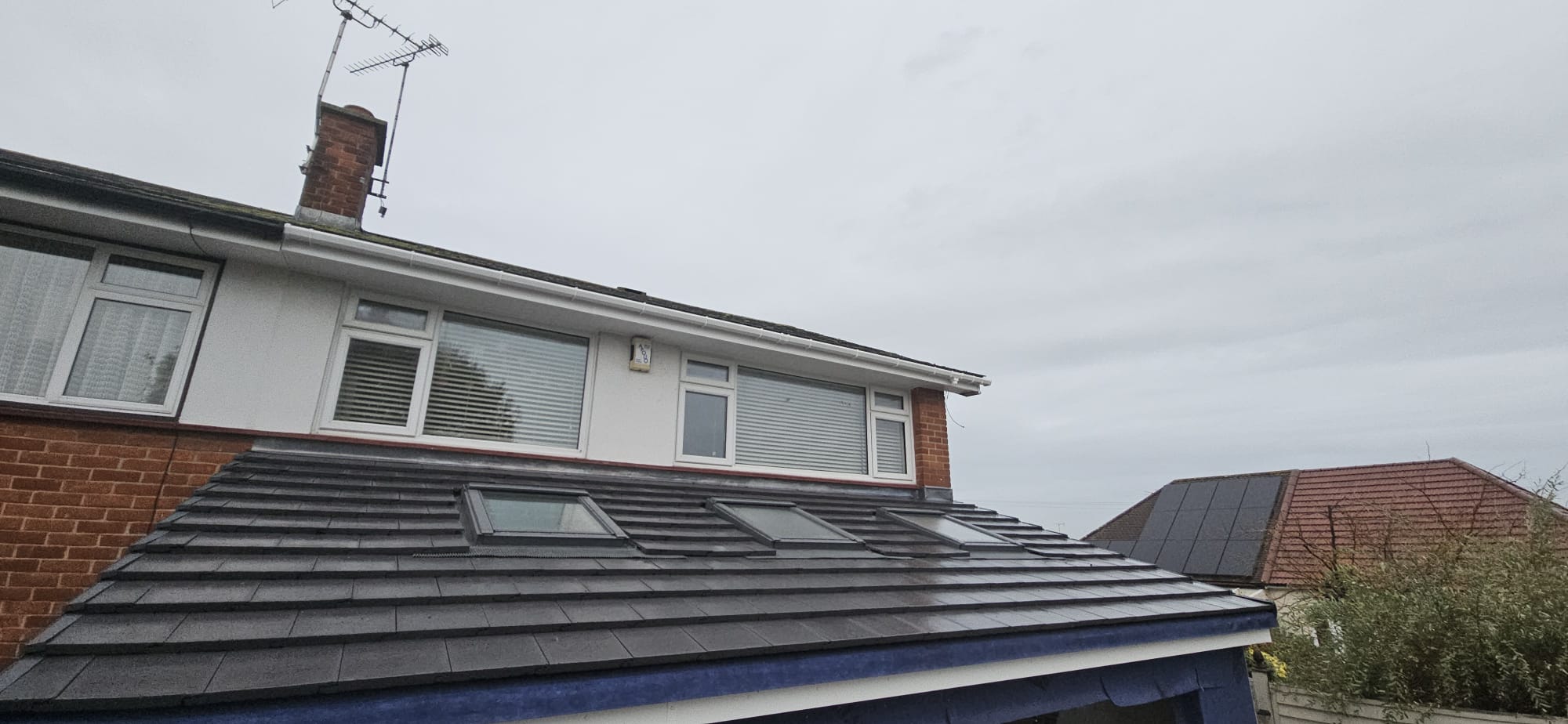 Newly tiled lean-to extension roof in dark grey tiles with three roof windows and lead flashing against the house wall